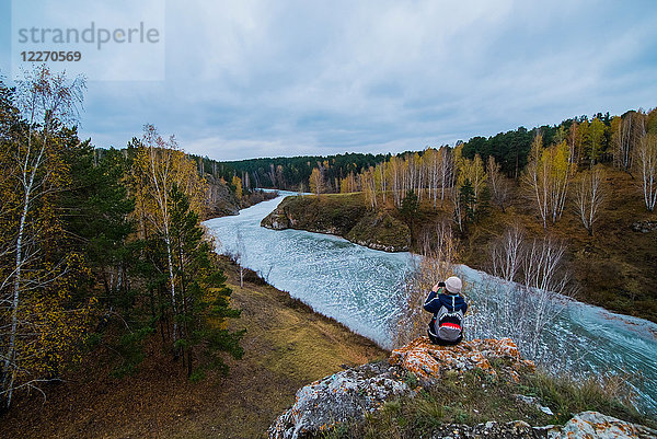 Rückansicht einer jungen Wanderin  die einen Fluss von Felsen aus fotografiert  Kislokan  Evenk  Russland