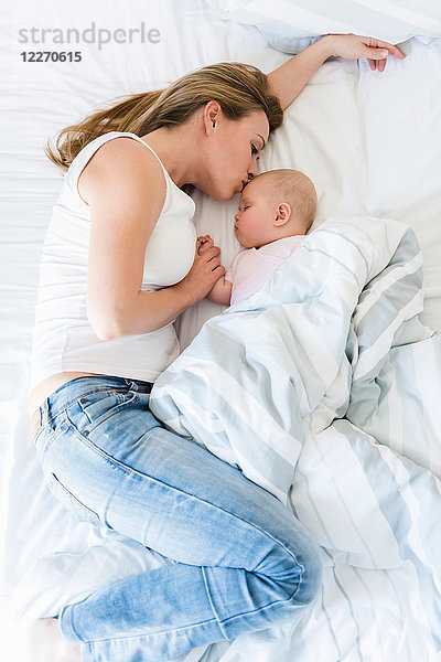 Mutter küsst schlafendes Baby im Bett