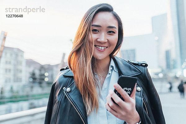 Porträt einer Geschäftsfrau im Freien  Smartphone in der Hand  lächelnd