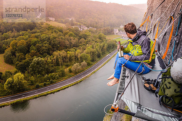 Junger männlicher Bergsteiger sitzend Felswand portaledge über der Maas  Freyr  Belgien  erhöhte Ansicht