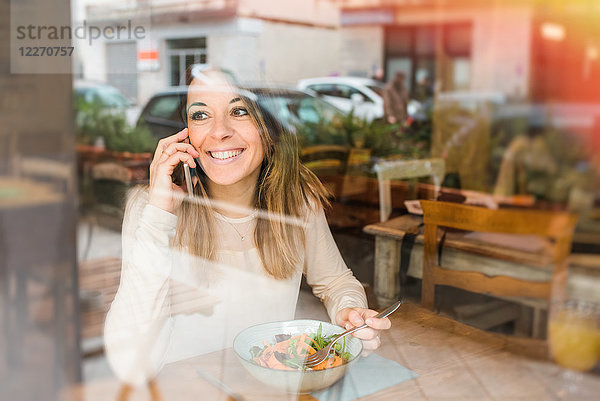 Frau benutzt Handy beim veganen Essen im Restaurant