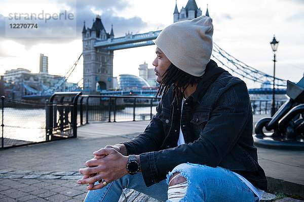 Junger Mann sitzt im Freien  nachdenkliche Mienen  Tower Bridge im Hintergrund  London  England  UK