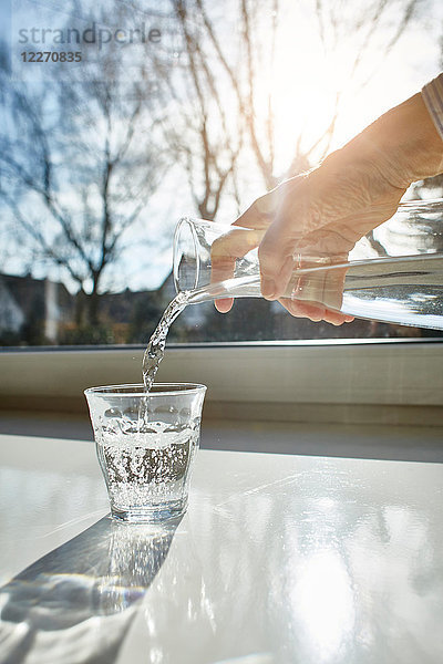Ältere Frau gießt ein Glas Wasser ein  Nahaufnahme