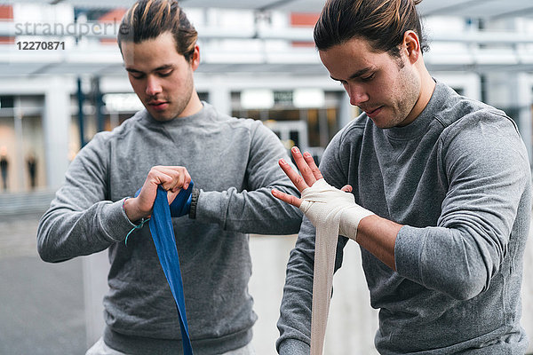 Identische männliche erwachsene Zwillingsboxer trainieren im Freien  bandagieren die Hände mit Handtuch