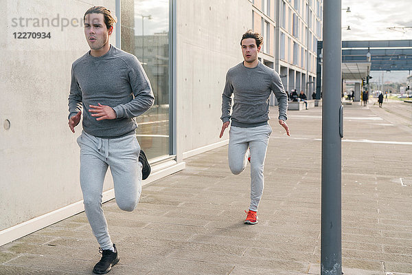 Junge erwachsene männliche Zwillingsläufer  die auf dem Bürgersteig der Stadt laufen