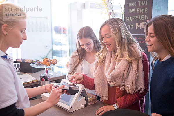 Freundinnen  die im Café am Tresen stehen und mit Kreditkarte bezahlen