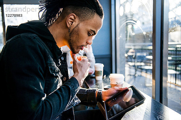Junger Mann sitzt im Café und schaut auf ein digitales Tablet  London  England  UK