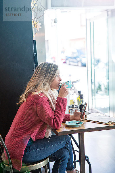 Frau sitzt im Café  trinkt Kaffee  hält Smartphone