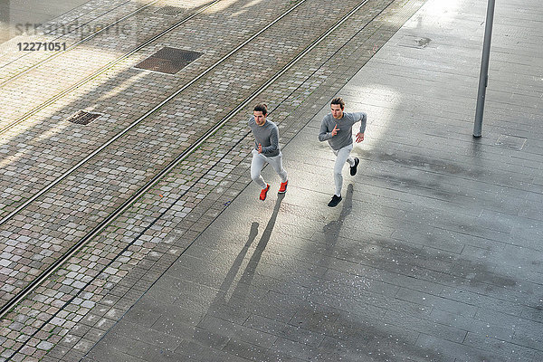 Junge erwachsene männliche Zwillinge  die zusammen laufen  entlang des Bürgersteigs laufen  Hochwinkelansicht