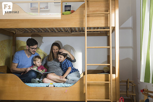 Vater und die schwangere Mutter lesen ihren beiden Söhnen auf dem Etagenbett ein Buch vor  München  Deutschland