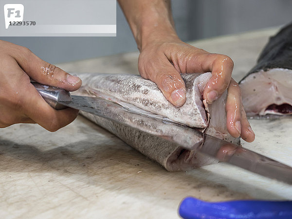 Mann schneidet Fisch mit Messer