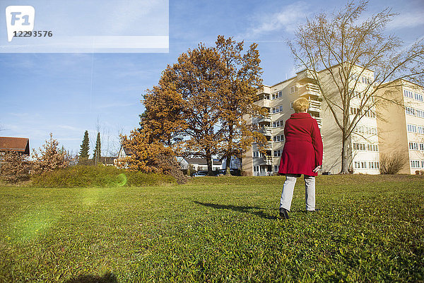 Alte Frau geht auf einer Wiese in der Nähe von Häusern spazieren