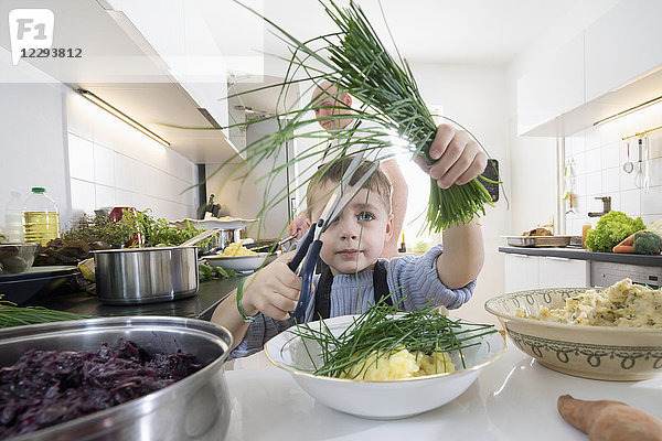 Kleiner Junge schneidet frischen Bio-Schnittlauch in der Küche