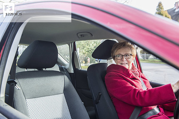 Glückliche alte Frau  die in einem Auto sitzt und aus dem Fenster schaut