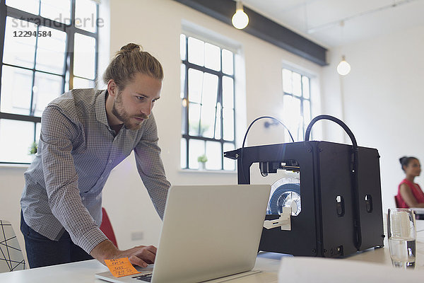 Männlicher Designer arbeitet am Laptop neben dem 3D-Drucker im Büro