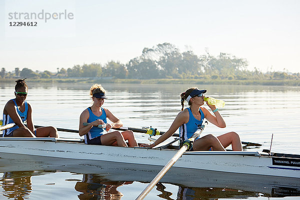 Weibliches Ruderteam ruht  Trinkwasser im Schädel auf dem sonnigen See