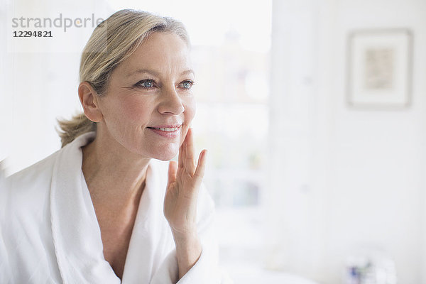 Lächelnde reife Frau  die sich vor dem Badezimmerspiegel mit Feuchtigkeitscreme eincremt
