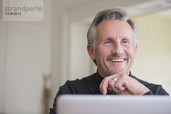 Lächelnder  selbstbewusster männlicher Freiberufler bei der Arbeit am Laptop