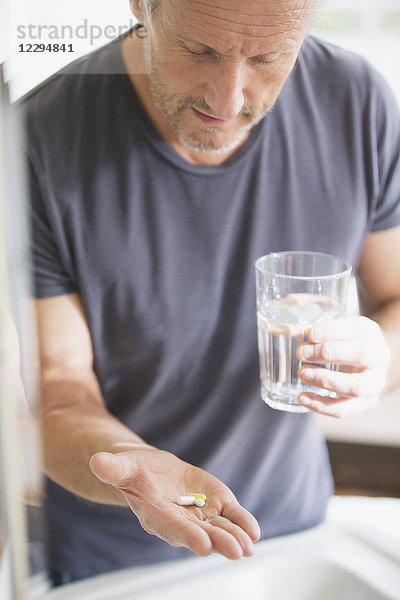 Älterer Mann nimmt Vitamine mit einem Glas Wasser ein