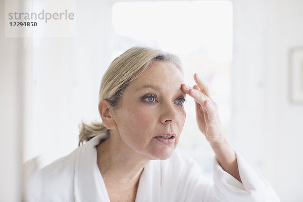 Reife Frau berührt Augenbraue im Badezimmerspiegel