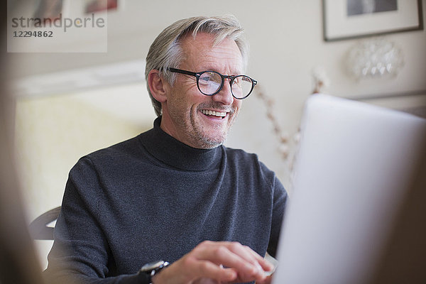 Lächelnder reifer männlicher Freiberufler arbeitet am Laptop