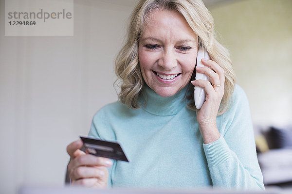 Lächelnde reife Frau mit Kreditkarte im Gespräch am Telefon