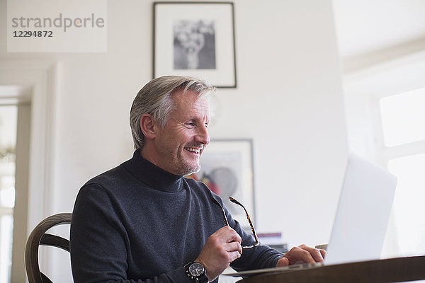 Lächelnder reifer männlicher Freiberufler  der zu Hause am Laptop arbeitet