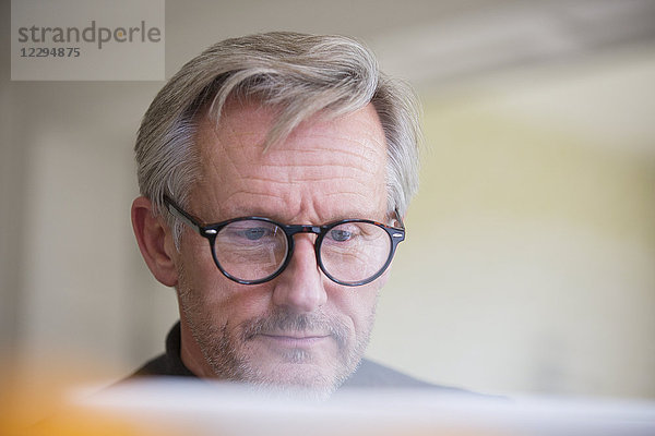 Fokussierter reifer Mann mit Brille arbeitet am Laptop