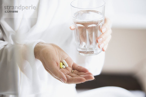 Frau nimmt Vitamine mit einem Glas Wasser ein