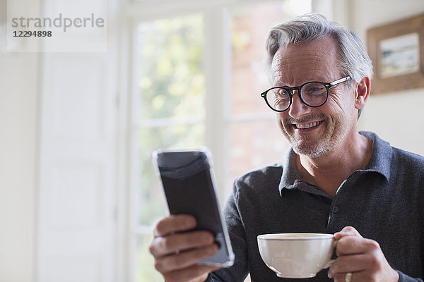 Lächelnder reifer Mann  der Tee trinkt und sein Smartphone benutzt