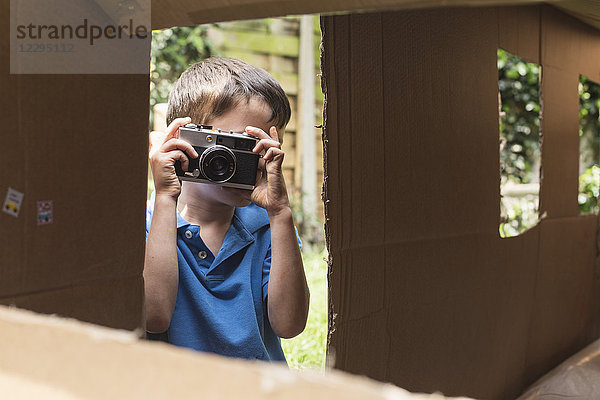 Junge fotografiert durch Pappspielhaus im Hinterhof