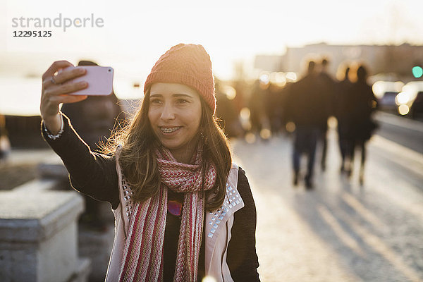 Lächelnde mittlere erwachsene Frau  die bei Sonnenuntergang Selfie vom Smartphone nimmt.