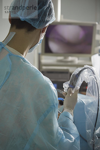 Rückansicht des männlichen Arztes  der die Geräte während der Operation im Operationssaal hält.