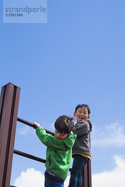 Flachwinkelansicht von Jungen  die auf Spielplatzgeräten gegen den blauen Himmel klettern.