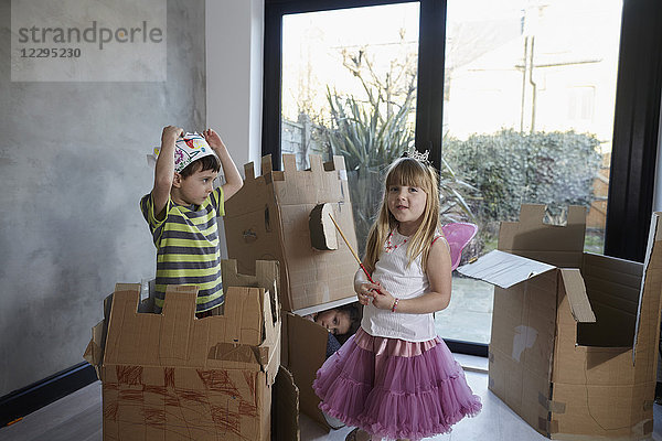 Kinder im Kostüm spielen mit Pappkartons gegen das Fenster