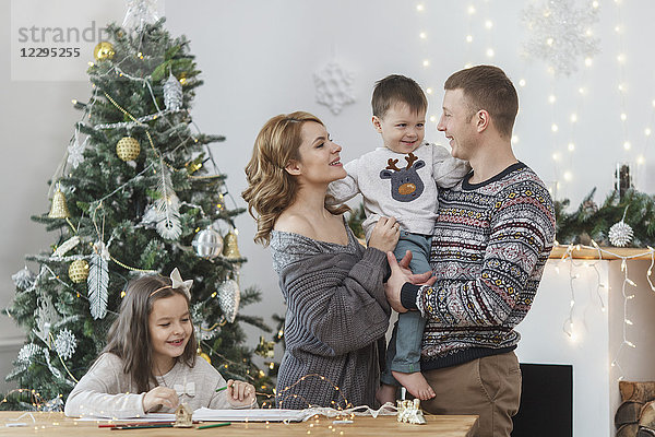 Vater und Mutter halten Sohn um Tochter am Tisch am Weihnachtsbaum sitzend