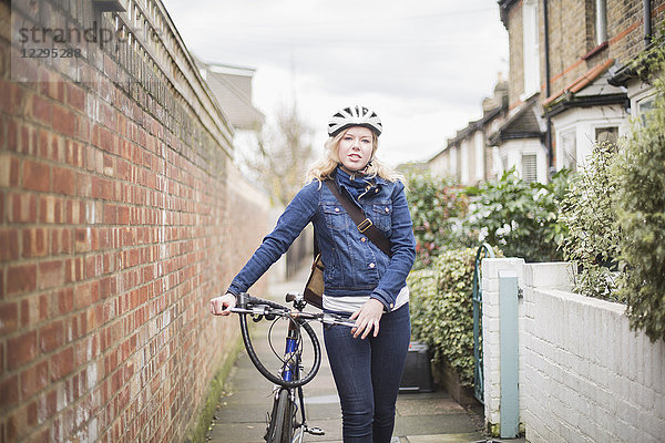 Porträt einer jungen Frau  die mit dem Fahrrad auf einem Wanderweg an der Wand spazieren geht.