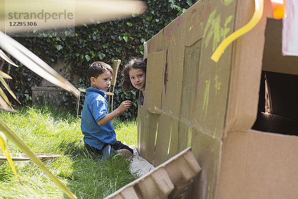 Elementare Freunde mit Pappspielhaus im Hinterhof an sonnigen Tagen