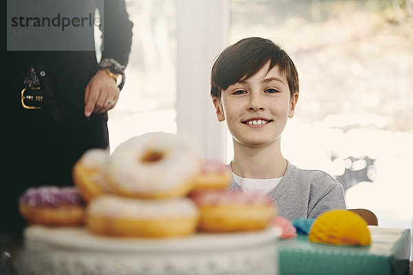 Portrait of smiling boy sitting by grandmother at dining table with donuts in foreground