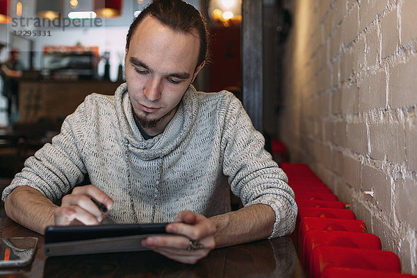 Junger Mann mit digitalem Tablett im Café