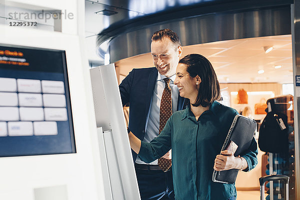 Happy business couple using self-service check-in machine at airport