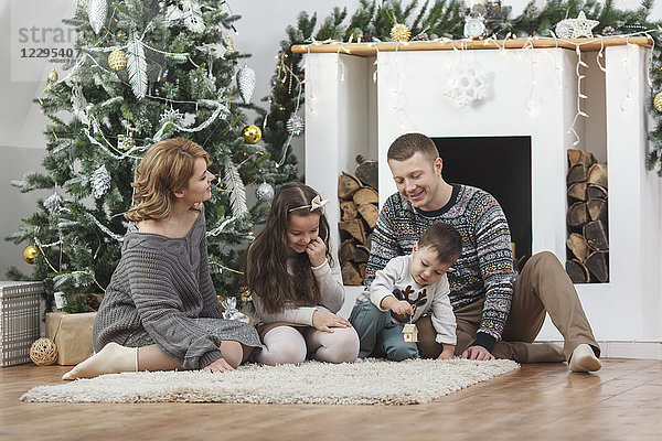 Glückliche Familie sitzend auf einem Teppich am Weihnachtsbaum zu Hause