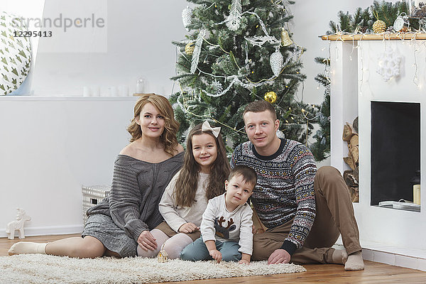 Porträt einer glücklichen Familie am Weihnachtsbaum sitzend