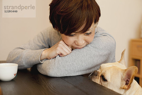 Frau sieht den Hund an  während sie sich auf den Tisch lehnt.