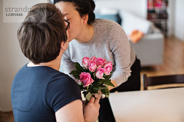 Close-up of lesbian couple kissing while holding pink roses at home