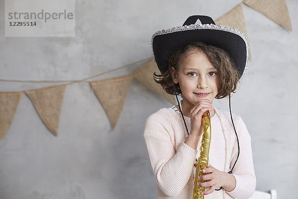 Porträt eines verspielten Mädchens mit Requisiten-Trompete an der verzierten Wand stehend
