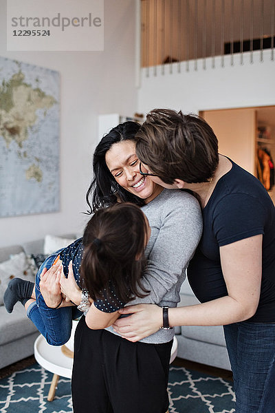 Woman kissing girlfriend with daughter in living room at home