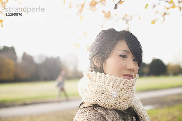 Nahaufnahme einer nachdenklichen jungen Frau mit Schal und Blick in den Park
