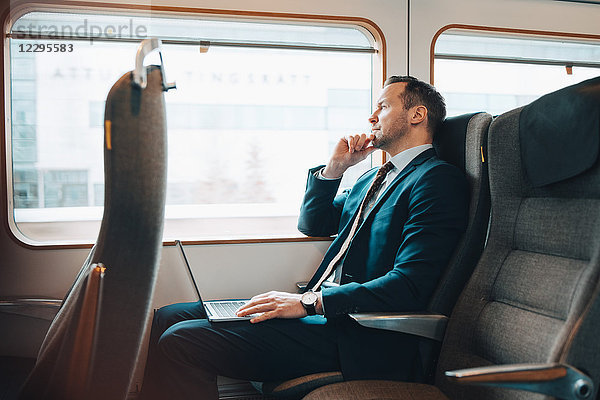 Thoughtful businessman with laptop traveling in train