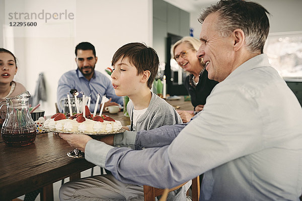 Boy blowing candles on birthday cake while sitting with family during party